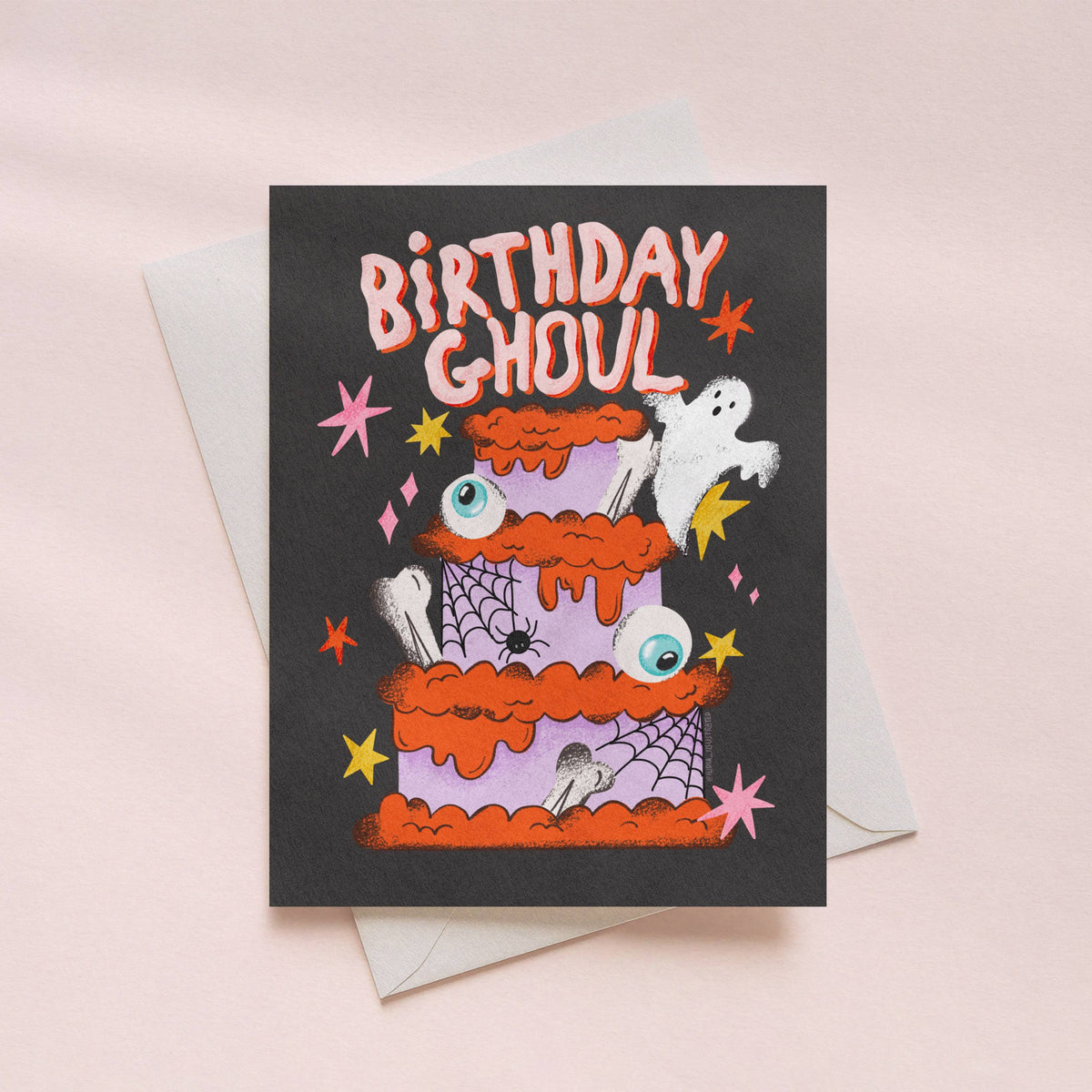 A Halloween-themed birthday card with a dark charcoal background, featuring a cartoon double-tiered orange cake with spiderwebs, eyeballs, and a white ghost. The text 'BIRTHDAY GHOUL' is written in orange at the top.