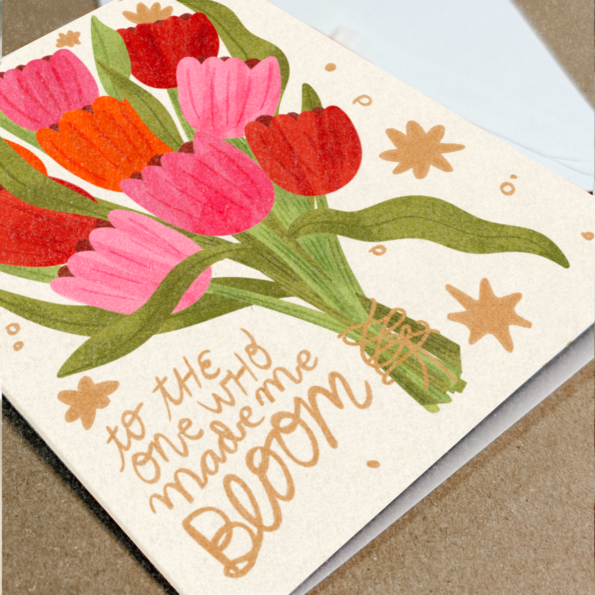 Greeting card with colorful tulips and text 'to the one who made me bloom' on a beige background.