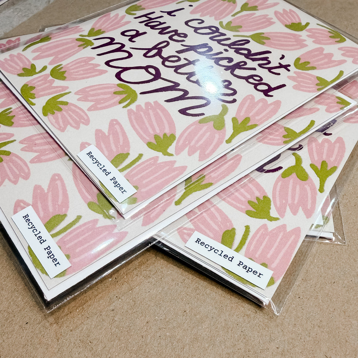Stack of greeting cards with pink tulip design and text on a brown surface