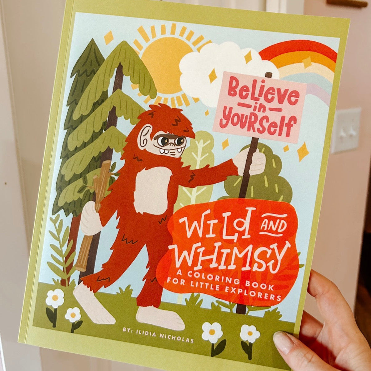 Coloring book titled 'Wild and Whimsy' held by a person with a cartoon character on the cover.