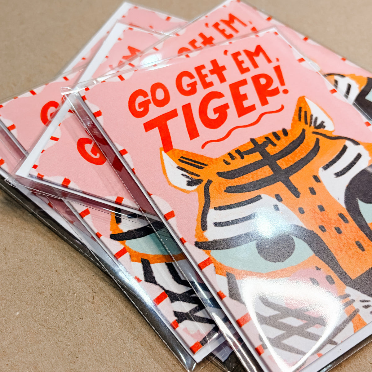 Stack of greeting cards with tiger design and 'Go Get Em Tiger!' text on a brown background