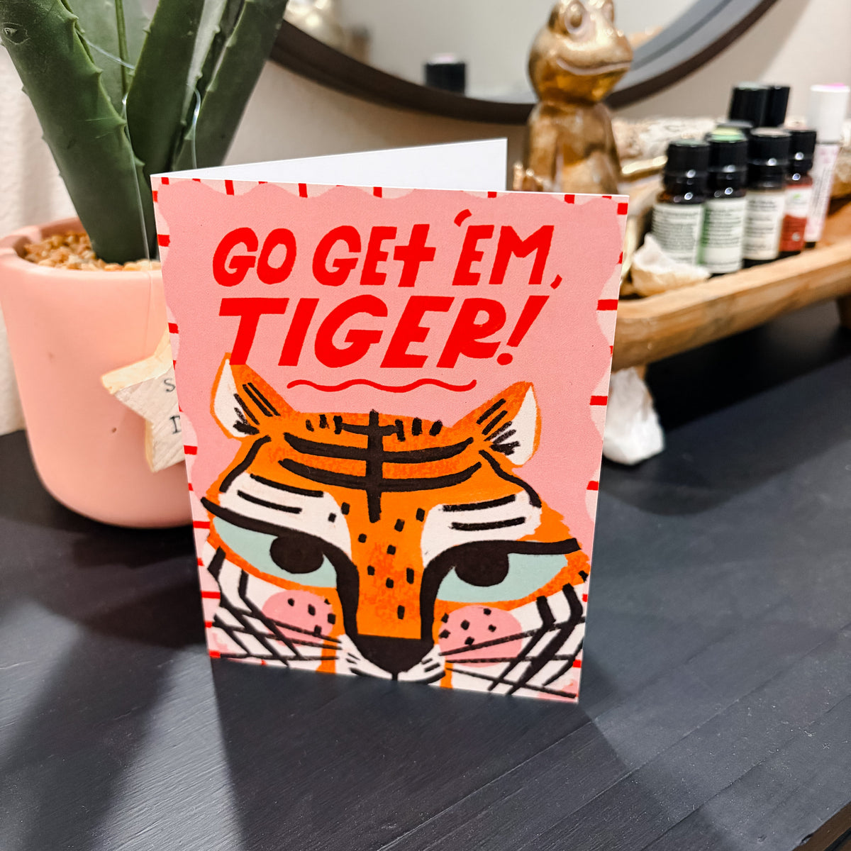 Card with tiger design and 'Go Get 'Em, Tiger!' text on a surface with a plant and bottles in the background