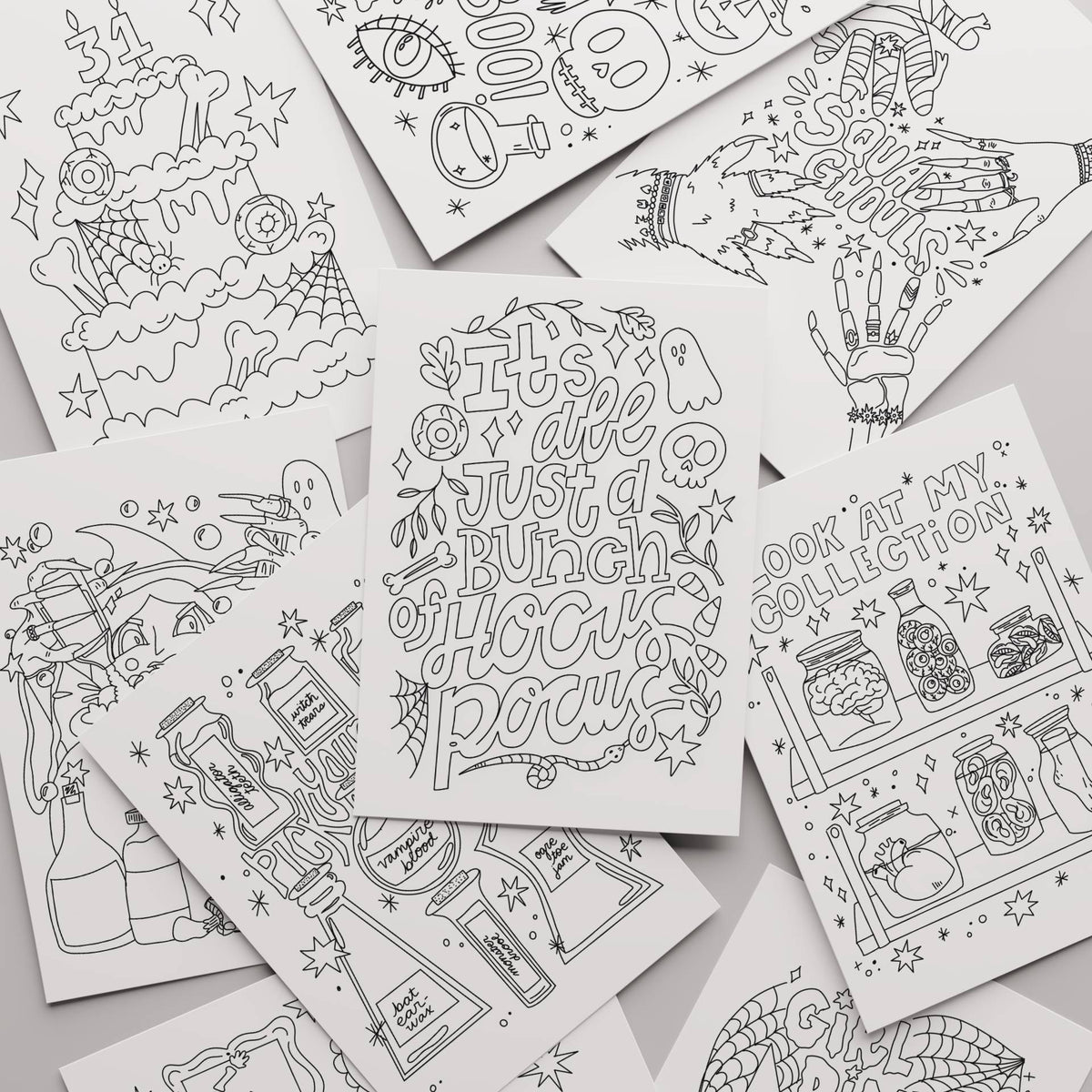A flat-lay collection of white coloring pages featuring black and white illustrations of witches, potion bottles, cauldrons, and spells, with one central page reading 'It's all just a bunch of hoohoo pocus'.