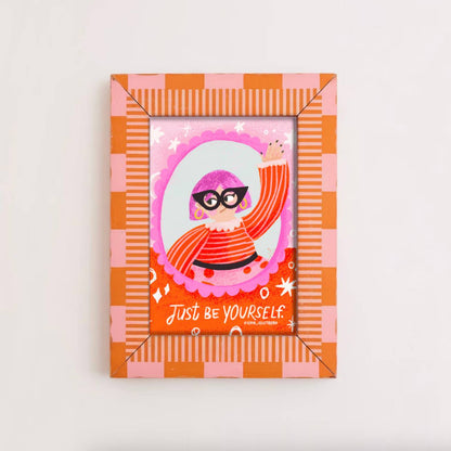 Framed artwork with a character illustration and 'Just be yourself' text on a checkered background.