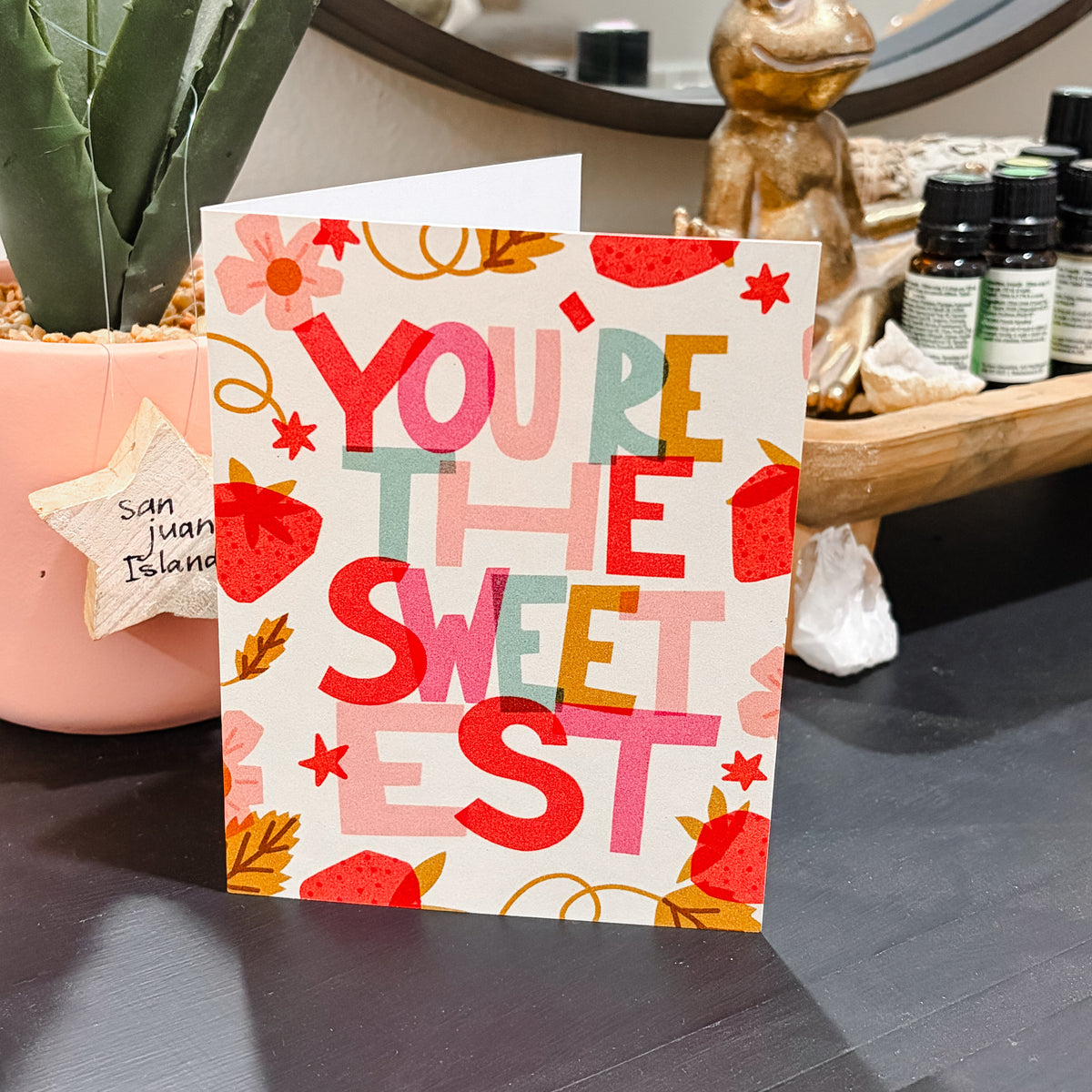 Card with 'You're the Sweetest' text on a surface with decorative items in the background