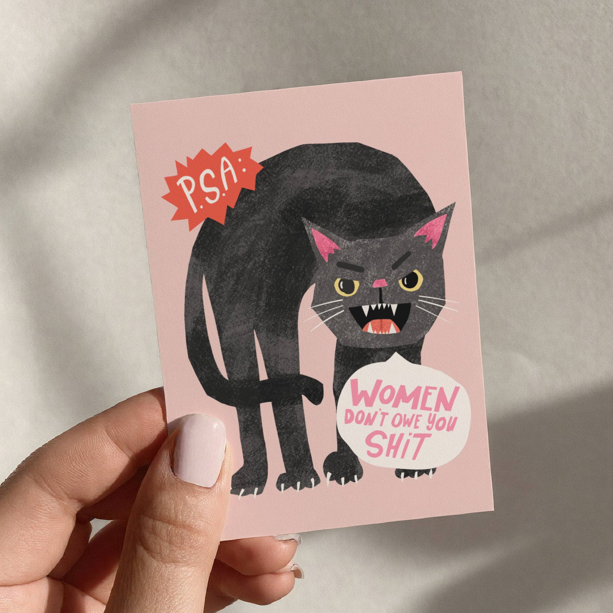 Card with a black cat illustration and text held by a hand against a neutral background