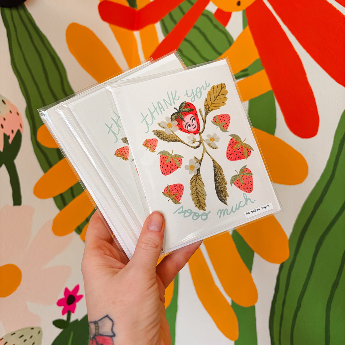 Hand holding a card with strawberry design against a colorful floral background