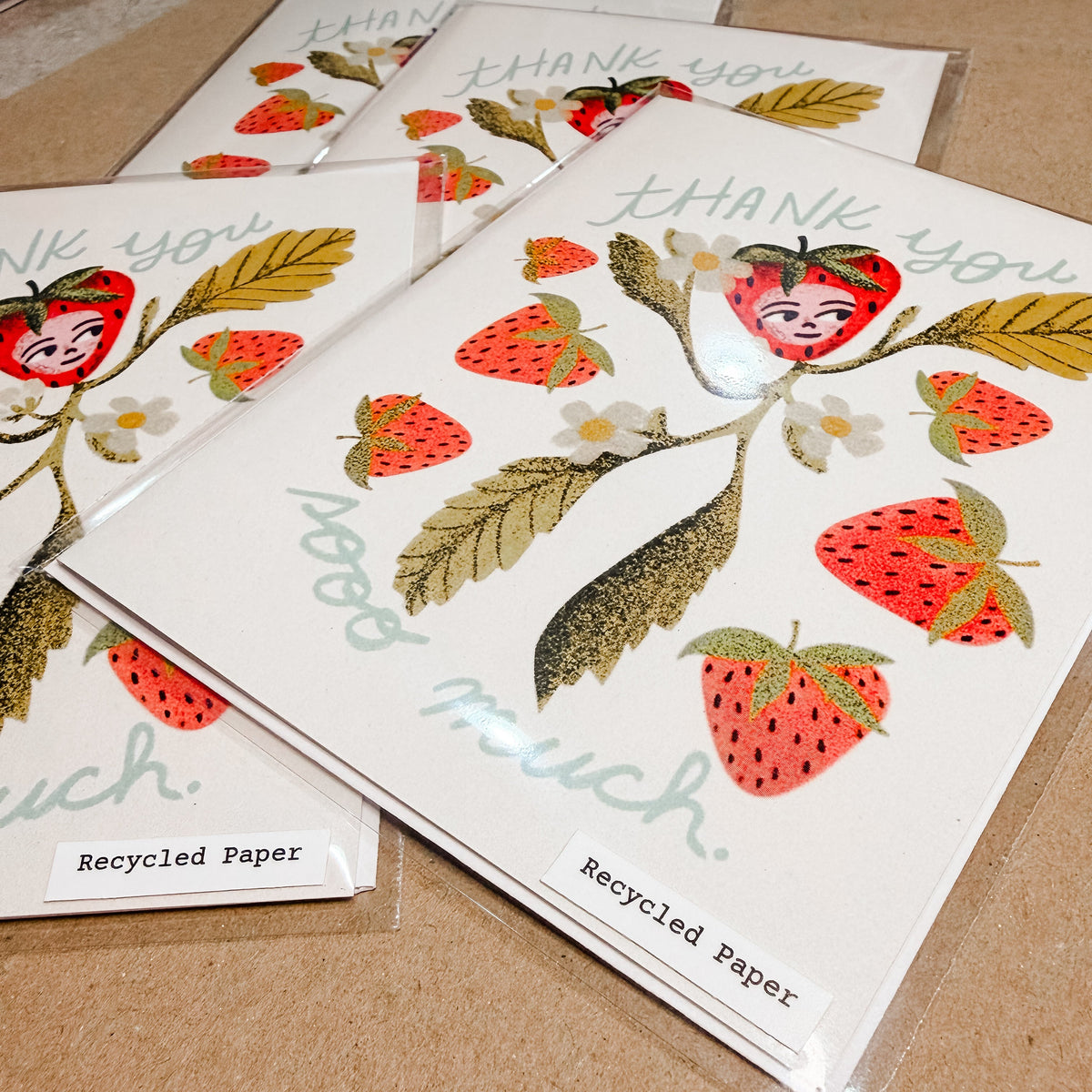 Stack of recycled paper thank you cards with strawberry design on a cardboard surface